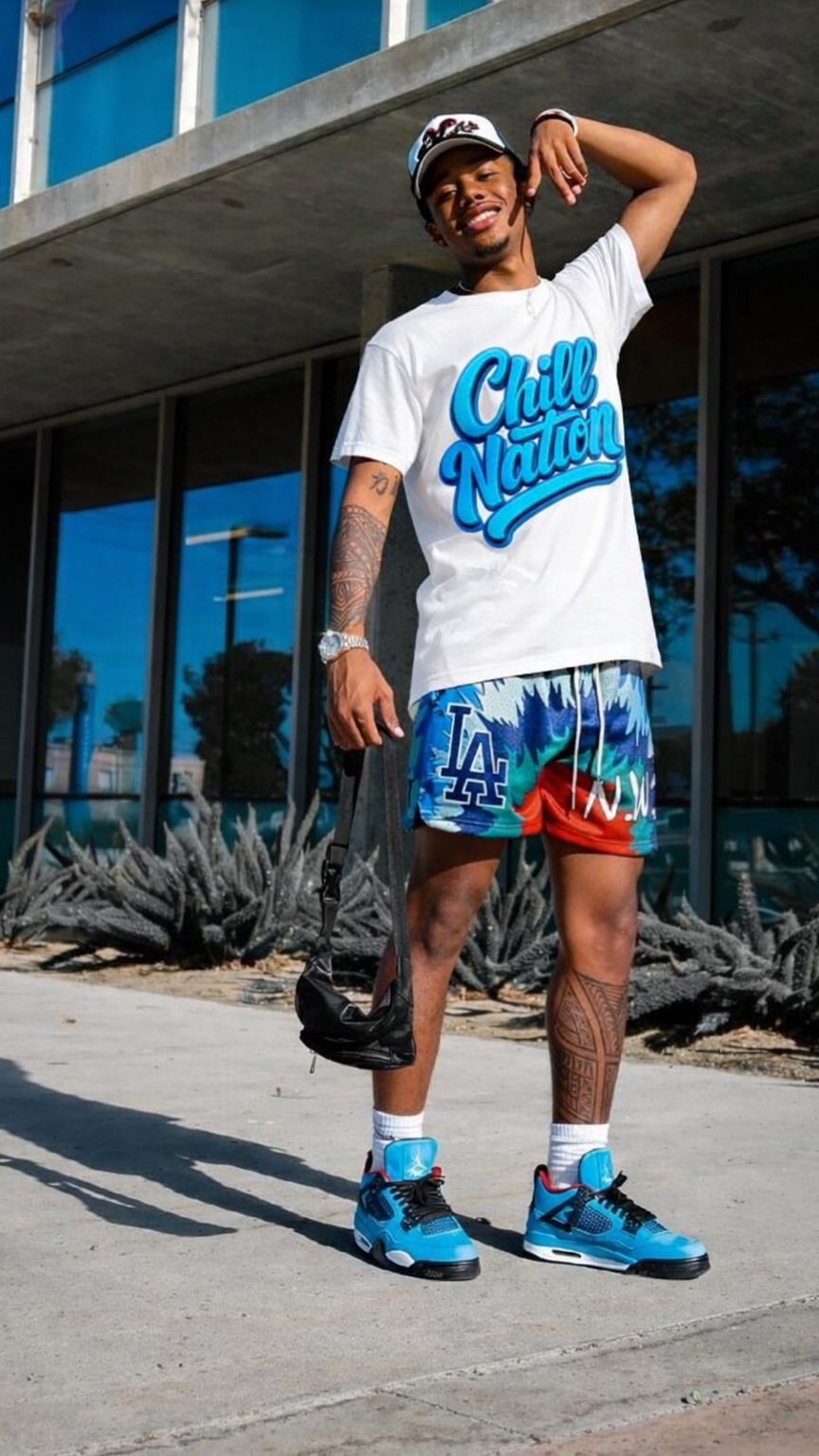 Person wearing a white t-shirt with blue text, colorful shorts, and blue sneakers standing on a sidewalk.